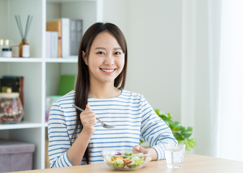 机の上にあるサラダを手に持ち微笑んでいる女性